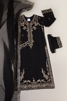 A pretty composition is layered over this elegant long silhouette on pure black cotton net. Featuring traditional paisleys with gold handwork details. Paired with embellished straight trousers and a matching ( gotah ) dupatta. A beautiful look for the festive season. Long Kameez length is 48 inches. -Fabric is pure han Black Semi-stitched Palazzo Set With Mirror Work, Black Palazzo Set With Gota Work For Eid, Black Palazzo Set With Gota Work For Festive Season, Black Palazzo Set With Gota Work For Festive Occasions, Festive Black Palazzo Set With Gota Work, Elegant Black Sharara With Gota Work, Black Chanderi Palazzo Set With Mirror Work, Designer Black Sharara With Gota Work, Elegant Black Salwar Kameez With Gota Work