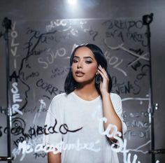 a woman standing in front of a wall with writing on it talking on a cell phone