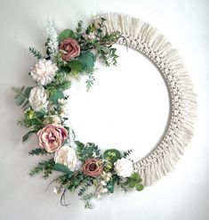 a circular wreath with flowers and greenery on the inside is hung on a white wall