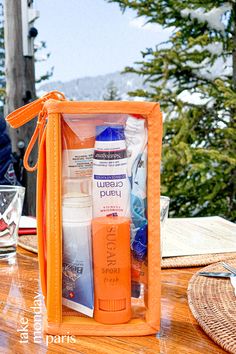 an orange box containing several different items on a wooden table with trees in the background