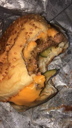 a hamburger with cheese and cucumbers on it sitting on tin foil covered in aluminum foil