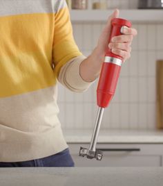 a woman is holding a red hand held blender in her hands while standing on the kitchen counter