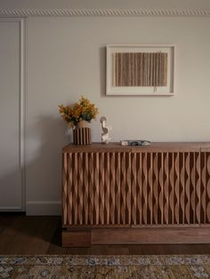 a wooden cabinet sitting on top of a hard wood floor next to a vase filled with flowers