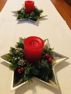 two red candles sit on top of a star shaped centerpiece with greenery and berries