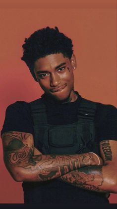 a man with tattoos on his arms posing for a photo in front of an orange background