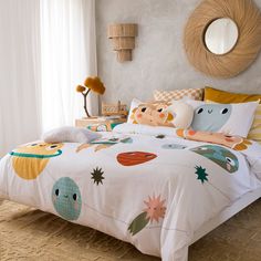 a bedroom with a bed covered in white sheets and colorful cartoon designs on the comforter