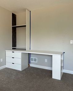 an empty room with a white desk and two drawers in the corner, on carpeted flooring