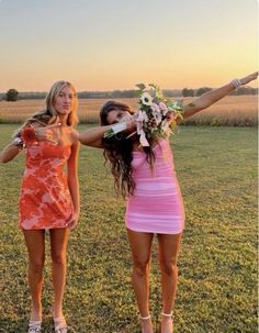 two beautiful young women standing next to each other on a lush green field at sunset