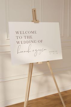 a welcome sign on an easel in front of a white wall and wooden floor