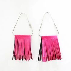 pair of pink and black fringe earrings hanging from metal hooks on white wall with clippings