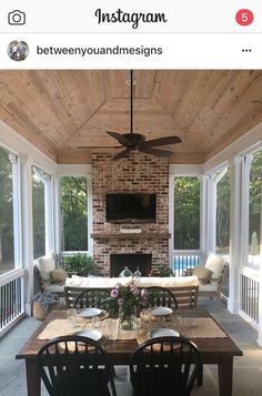 an enclosed patio with table, couches and television on the wall in front of fireplace