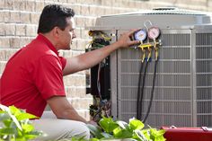 a man fixing an air conditioner in front of a brick wall with green plants