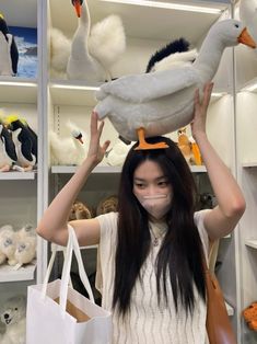 a woman holding a stuffed duck on her head in front of shelves filled with stuffed animals