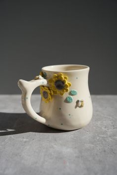 a white ceramic cup with yellow flowers on it's handle and handles, sitting on a table