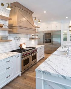 a kitchen with marble counter tops and stainless steel oven hoods, white cabinets, and wood flooring