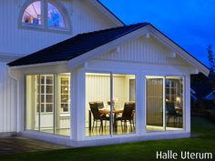 a house that is lit up at night with the lights on and dining table outside