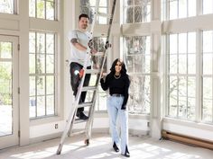 a man and woman are standing on a ladder in front of large windows while another person stands next to them