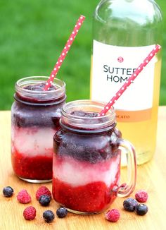 two mason jars filled with raspberry and blueberries next to a bottle of rum