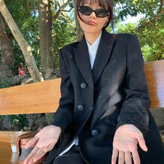 a woman sitting on top of a wooden bench wearing sunglasses and holding her hands out