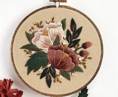 a close up of a embroidery on a white surface with flowers in the center and leaves around it