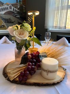 a table topped with a vase filled with flowers next to a candle and some grapes