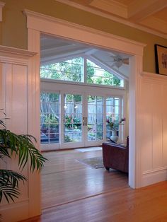 a living room filled with furniture and lots of windows next to a wooden floor covered in plants