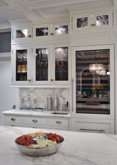 a bowl of fruit is sitting on the counter in this kitchen with white cabinets and marble counter tops