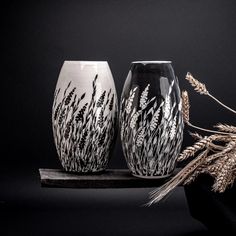 two black and white vases sitting next to each other on a wooden stand with dried grass