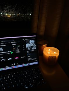 an open laptop computer sitting on top of a wooden desk next to a lit candle