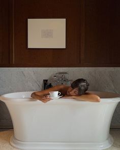 a woman laying down in a bathtub with her head resting on a coffee cup