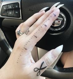 a woman's hand with scissors tattooed on her left thumb and fingers in front of the steering wheel