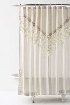 a white shower curtain with an embroidered design on the top and bottom, hanging from a metal rod