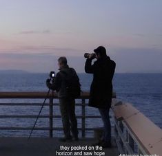 two people standing on a pier looking out at the ocean with cameras in front of them