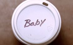 a white cup with the word baby painted on it's lid sitting on a table