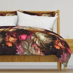 a bed with a flowered comforter and pillows on top of it, in front of a white wall