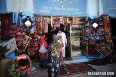 two people standing in front of a shop selling rugs and other items on display