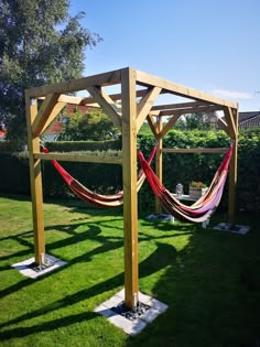 an outdoor hammock set up in the grass next to a wooden structure with two hammocks hanging from it's sides