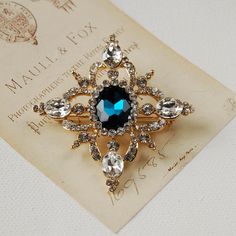 This elegant, vintage style brooch features a statement blue stone surrounded by sparkling diamante gems. Sure to add a touch of sparkle to any outfit, it is a lovely reproduction piece and would make a gorgeous gift for a mother, sister or special friend. The brooch is gift-wrapped in white tissue and comes in an exclusive Carriage Trade gift box free of charge. Metal alloy brooch with diamante and glass stones, measures 5cm at its widest point. Blue stone 1.5cm by 1cm. Elegant Blue Brooch Pins, Elegant Blue Brooch, Elegant Blue Wedding Brooches, Gold Brooches, Engraved Gifts, Childrens Jewelry, Wedding Keepsakes, Gorgeous Gift, Special Friend