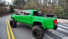 a green pick up truck parked on the side of a road with trees in the background