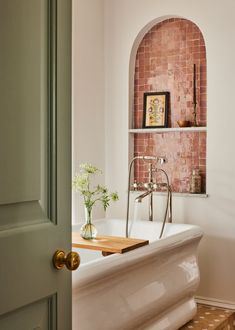 a bath tub sitting under a window next to a wooden shelf filled with vases