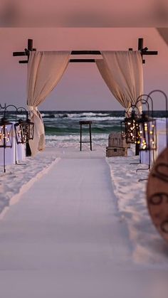 an outdoor ceremony set up on the beach with candles and drapes draped over it