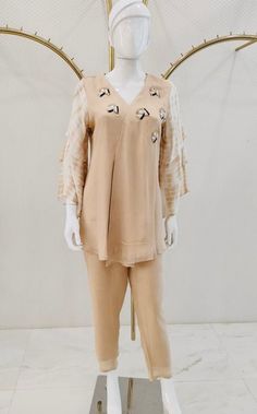 A peach colored kurta and palazzo set, curated for a casual evening affair, is fashioned from luxurious fabric to guarantee comfort. The short kurti, adorned with embroidered buttis scattered around the neck and featuring elbow-length 3 tier sleeves, exudes an understated elegance. The ensemble is impeccably completed by plain straight pants in matching colors, presenting a cohesive and sophisticated look.  Note: Colors may slightly vary due to photographic lighting. Please contact us if you hav Designer Spring Kurta With Set-in Sleeves, Designer Wear Spring Kurta With Set-in Sleeves, Summer Straight Kurta With Set-in Sleeves, Elegant Summer Kurta With Set-in Sleeves, Spring Festive Palazzo Set With Set-in Sleeves, Designer Long Sleeve Pant Set For Spring, Summer Beige Pant Set, Spring Designer Wear Sharara With Straight Kurta, Designer Straight Kurta Pant Set For Spring