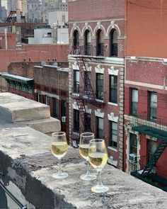 two glasses of wine sitting on top of a cement ledge in front of a brick building