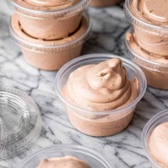 several plastic containers filled with chocolate frosting on a marble counter top next to plates