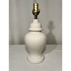 a white table lamp with a gold colored light bulb on it's top and bottom