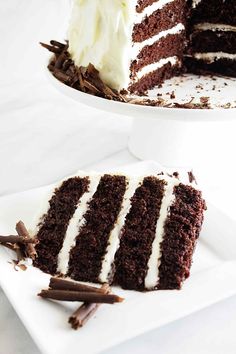 a slice of chocolate cake with white frosting on a serving platter and the rest of the cake in the background