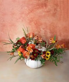 a white vase filled with lots of flowers on top of a table next to a wall