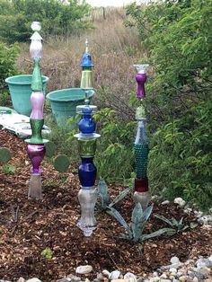 several colorful vases sitting on top of a pile of dirt next to trees and bushes