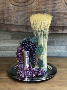 a metal plate topped with grapes next to a vase filled with wheat stalks and leaves