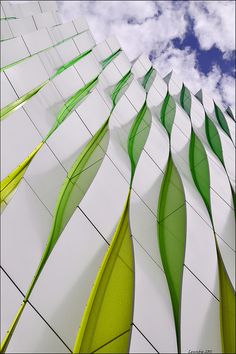 an architectural building with green and white wavy lines on it's side, against a cloudy blue sky